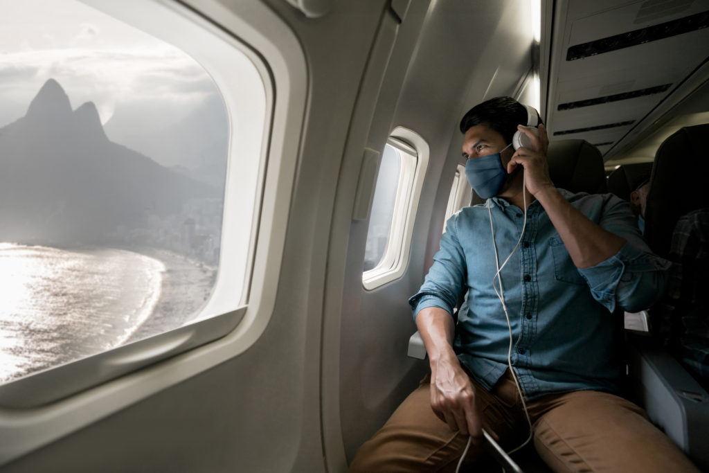 Man traveling by plane wearing a facemask and looking at Rio through the window