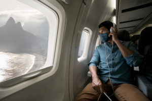 Man traveling by plane wearing a facemask and looking at Rio through the window
